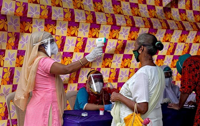 A health worker wearing protective face mask and face shield checks the temperature of a resident during a check-up campaign for the coronavirus disease (COVID-19) in Mumbai, India.  REUTERS